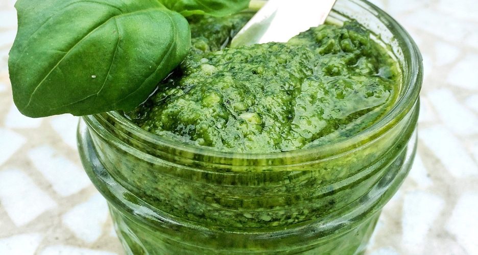Świeże pesto bazyliowe w słoiku z łyżką i listkami bazylii.