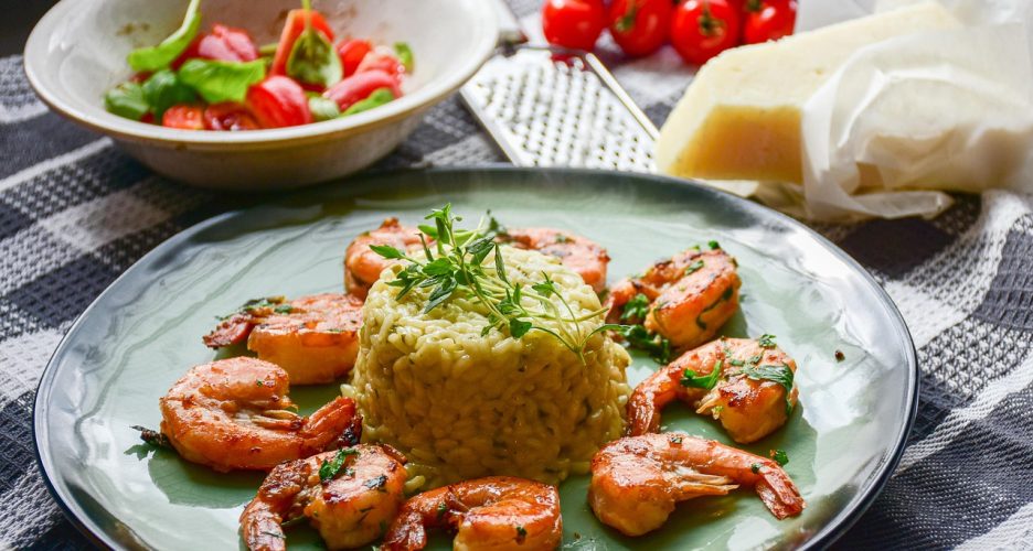 Talerz z kremowym risotto otoczonym krewetkami, podany z parmezanem i pomidorkami.